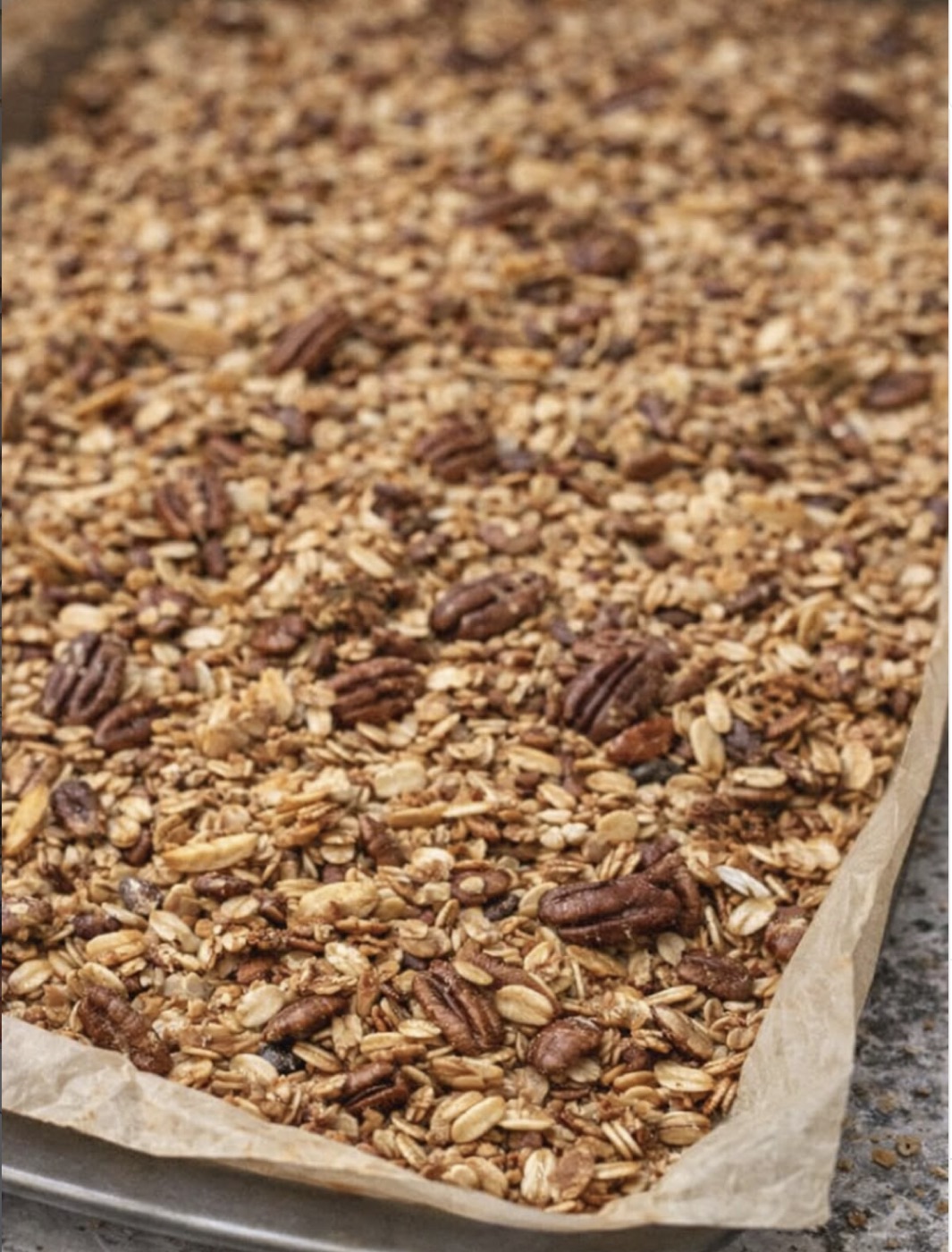 A tray of freshly baked granola with pecans, cooling on parchment paper